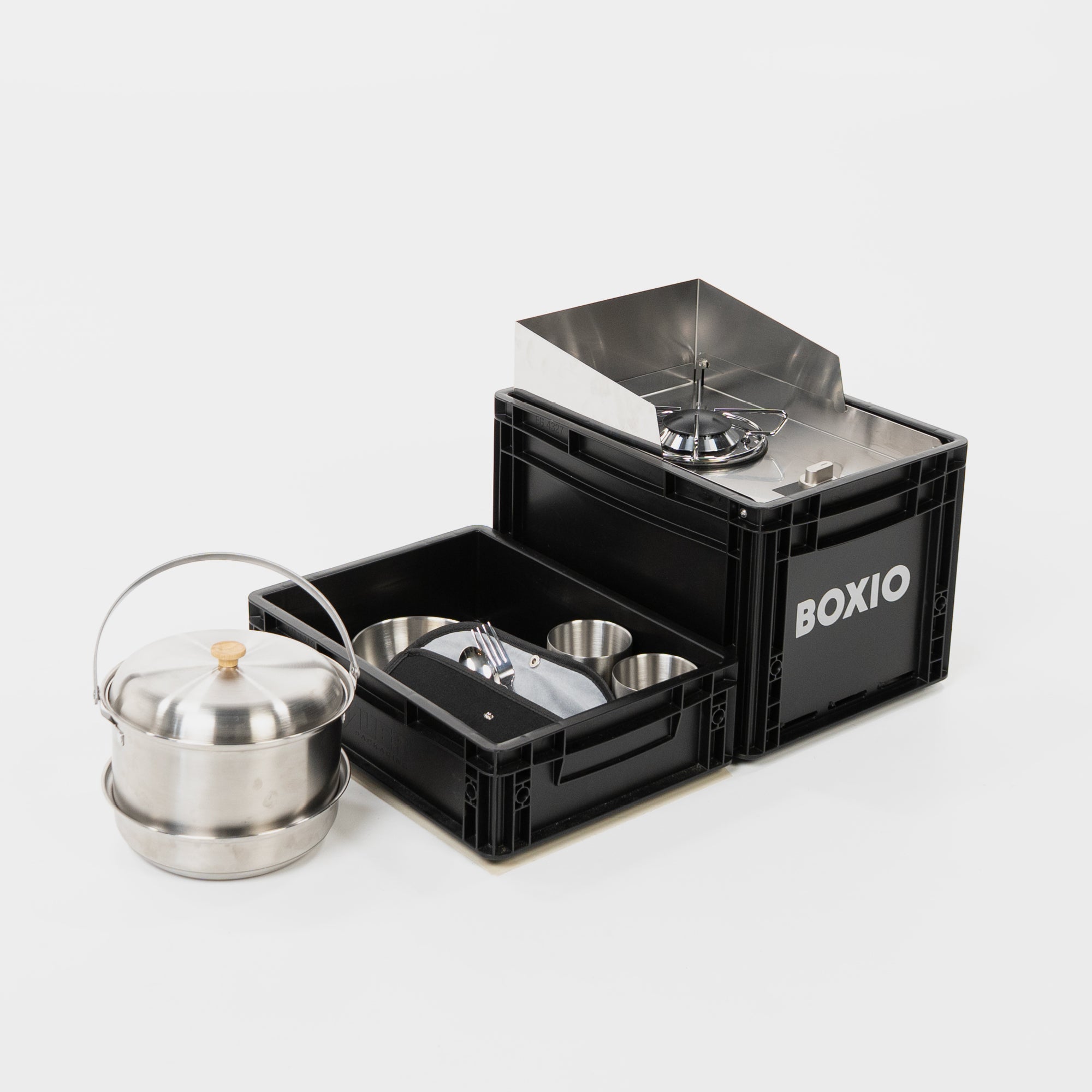 nebeneinander platziert sind Campingtopfset, halbe Eurobox mit Geschirr und Besteck und mobiler Gaskocher