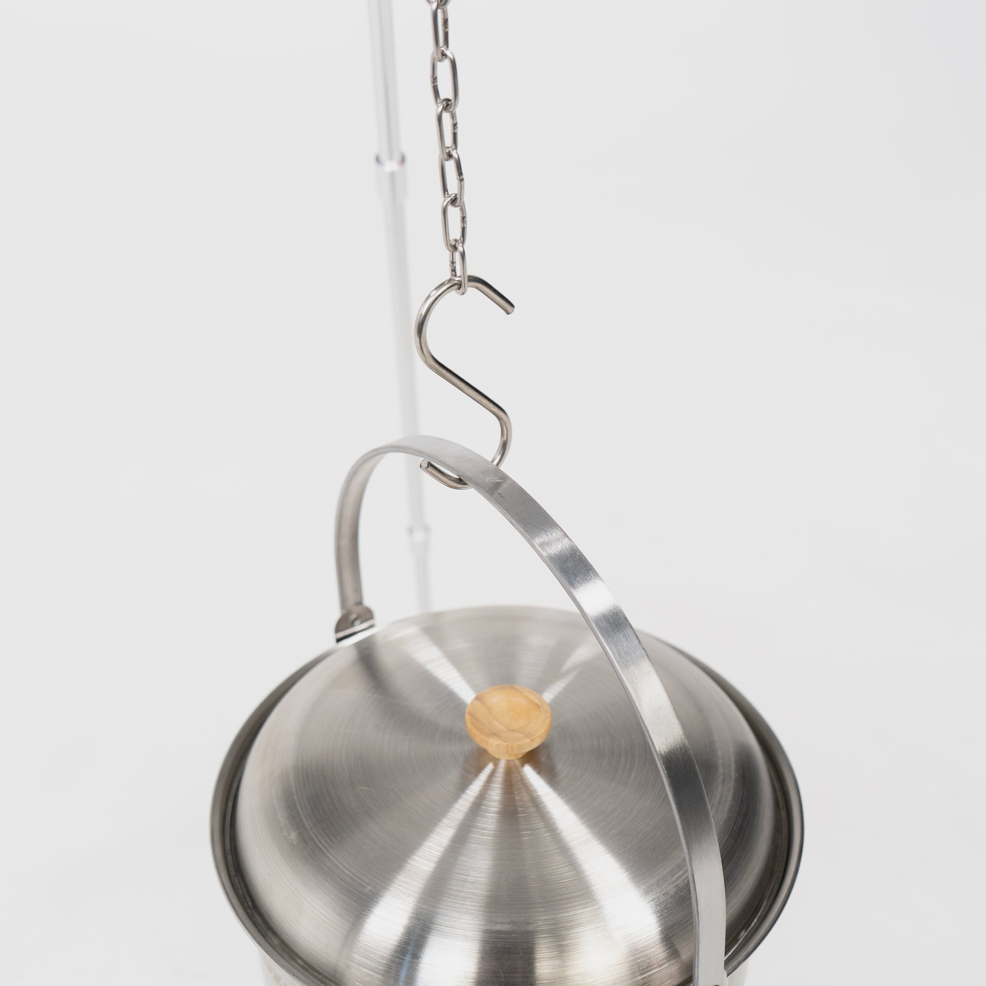 Edelstahl-Topf mit Holzgriff, aufgehängt an einer Kette mit einem S-Haken, vor weißem Hintergrund.