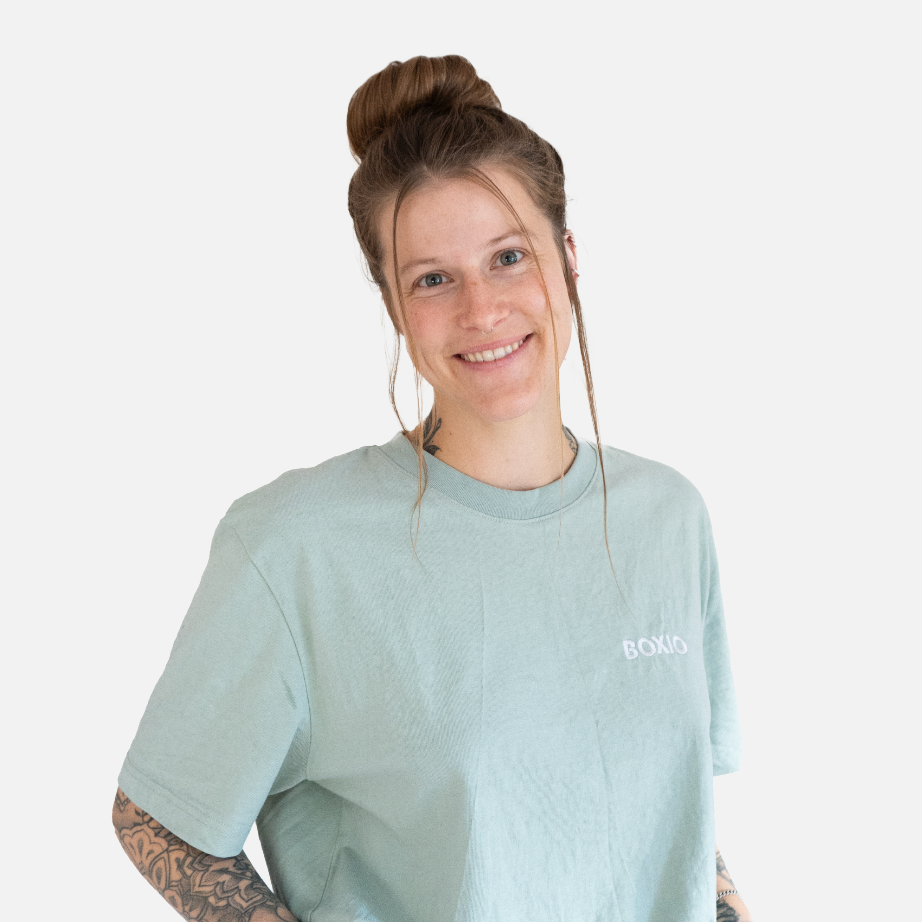 Lächelnde Person mit Hochsteckfrisur trägt ein mintgrünes T-Shirt und zeigt ihre Tätowierungen.