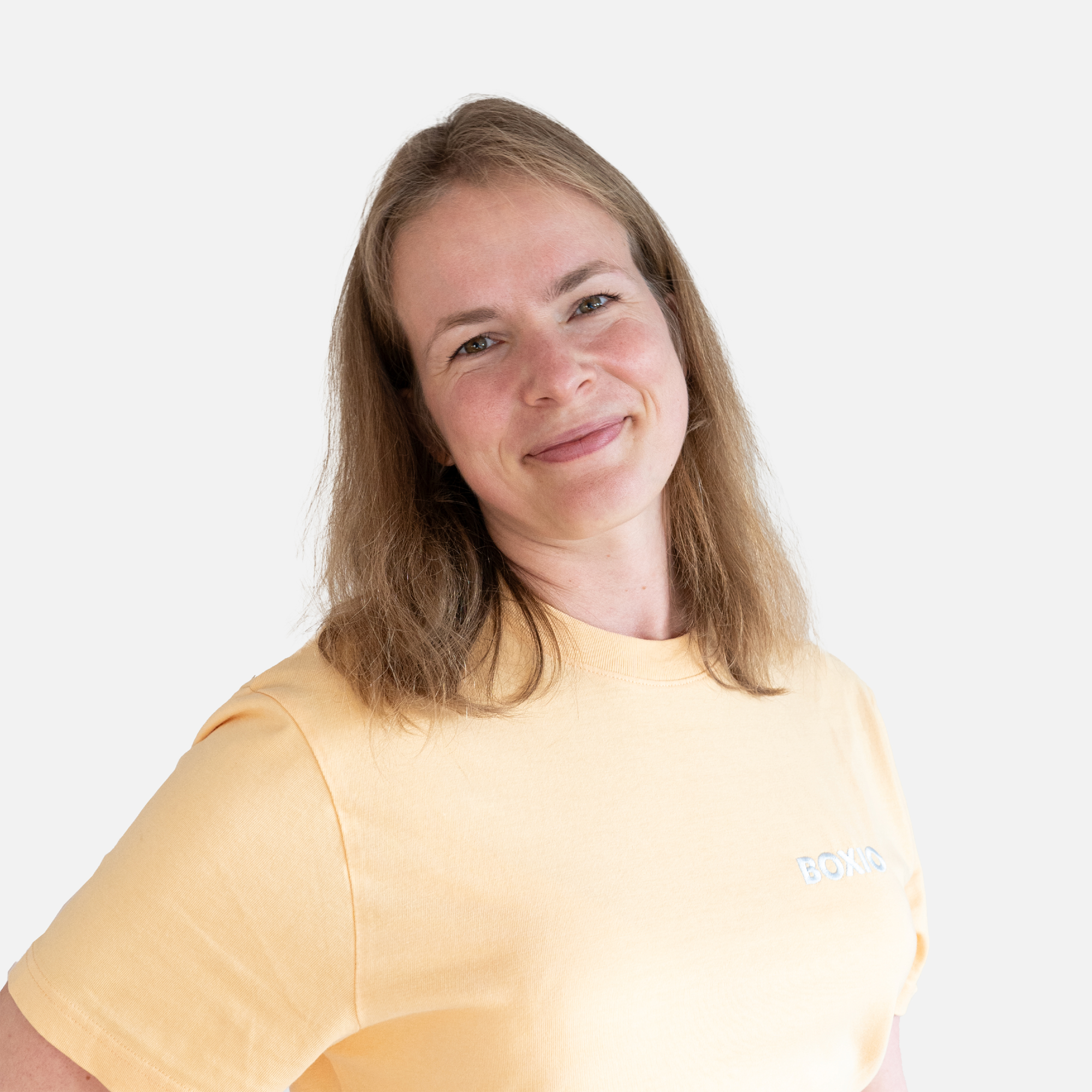 Junge Frau mit halblangem Haar in einem gelben T-Shirt, lächelt freundlich vor einem neutralen Hintergrund.