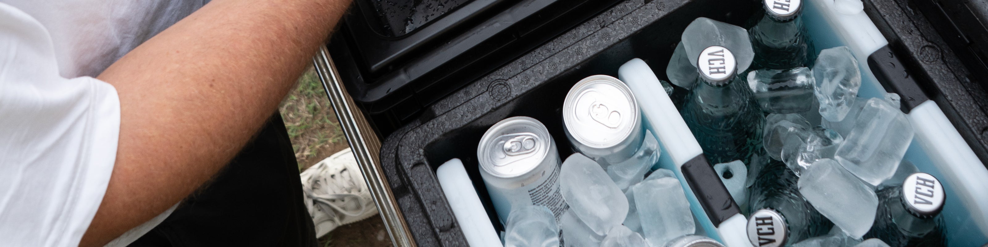 Kühlbox mit Eiswürfeln und Getränkedosen, während jemand die Box öffnet.