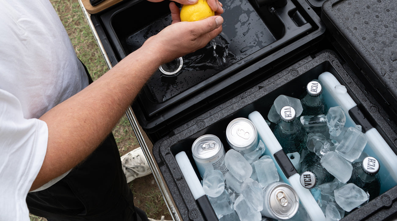Eine Person presst eine Zitrone über einem funktionalen Kühlbehälter, der mit Eis und Getränkedosen gefüllt ist.