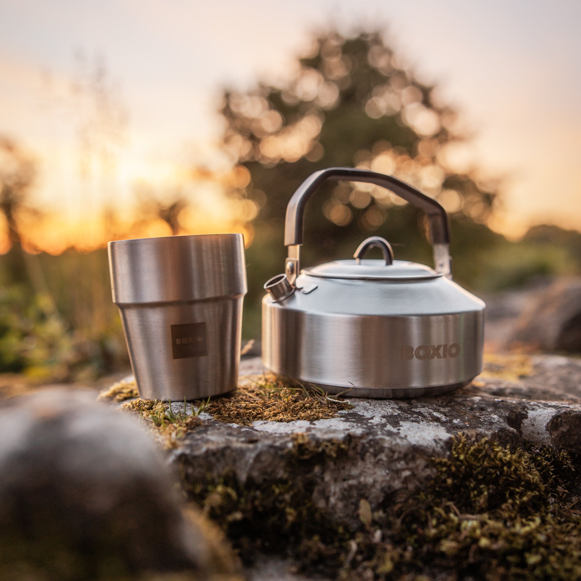 Wasserkessel und Camping Trinkbecher auf einem Stein mit Wald im Hintergrund 