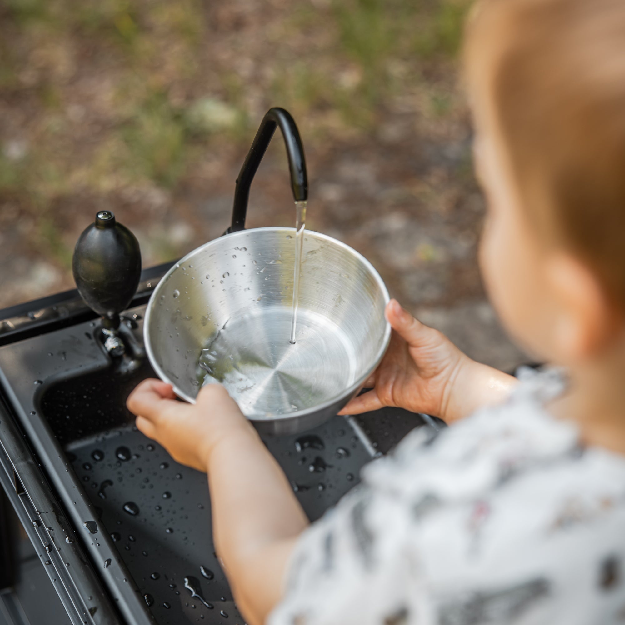Kind hält eine Edelstahlschüssel unter den Wasserhahn eines mobilen Waschbeckens 